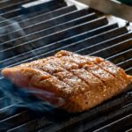 Close-up of a juicy salmon fillet sizzling on an outdoor grill, surrounded by aromatic smoke.