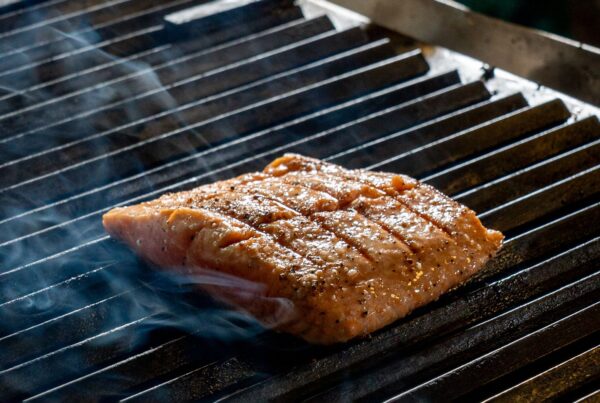 Close-up of a juicy salmon fillet sizzling on an outdoor grill, surrounded by aromatic smoke.
