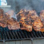 Close-up of delicious grilled ribs smoking on a barbecue grill, perfect for a summer cookout.